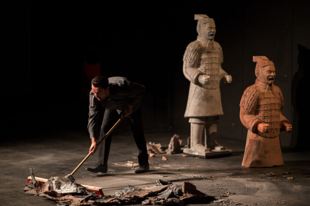 Mężczyzna (Arti Grabowski) zamiatający elementy scenografii miotłą podczas spektaklu Warunki zabudowy